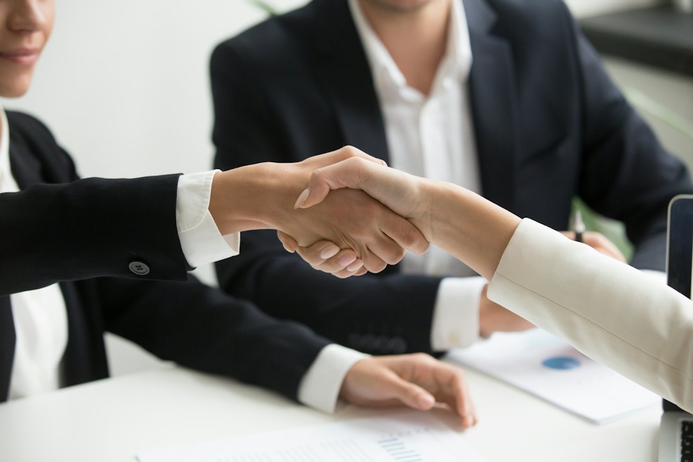 Two people shaking hands over a laptop