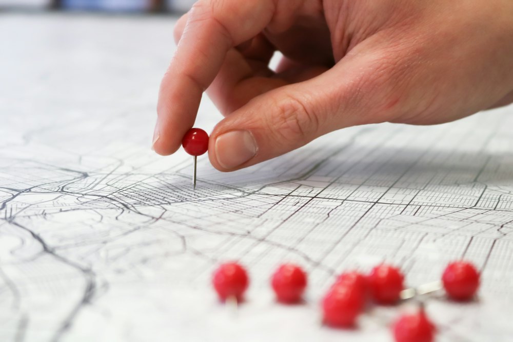 A hand placing a red pin on a city map